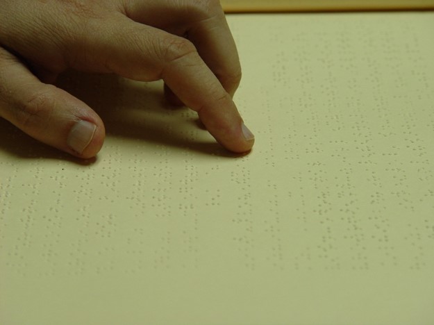 Foto de una mano leyendo Braille sobre un papel.